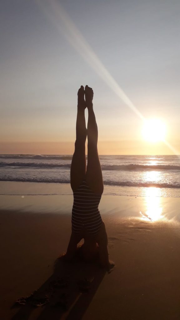 Carole pratique la posture de yoga Sirsasana sur la plage